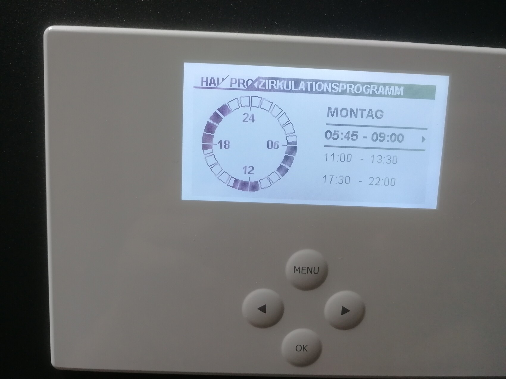 Medizinisches Gerät mit Display: Uhrkreis-Diagramm und Montag-Programmzeiten; MENU/OK-Tasten.
