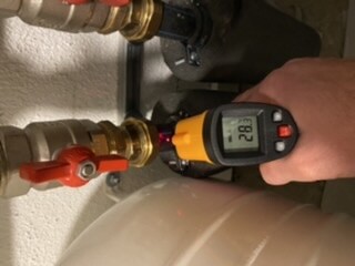 Hand hält digitales Thermometer an Haustechnikrohren unter dem Spuelenschrank.