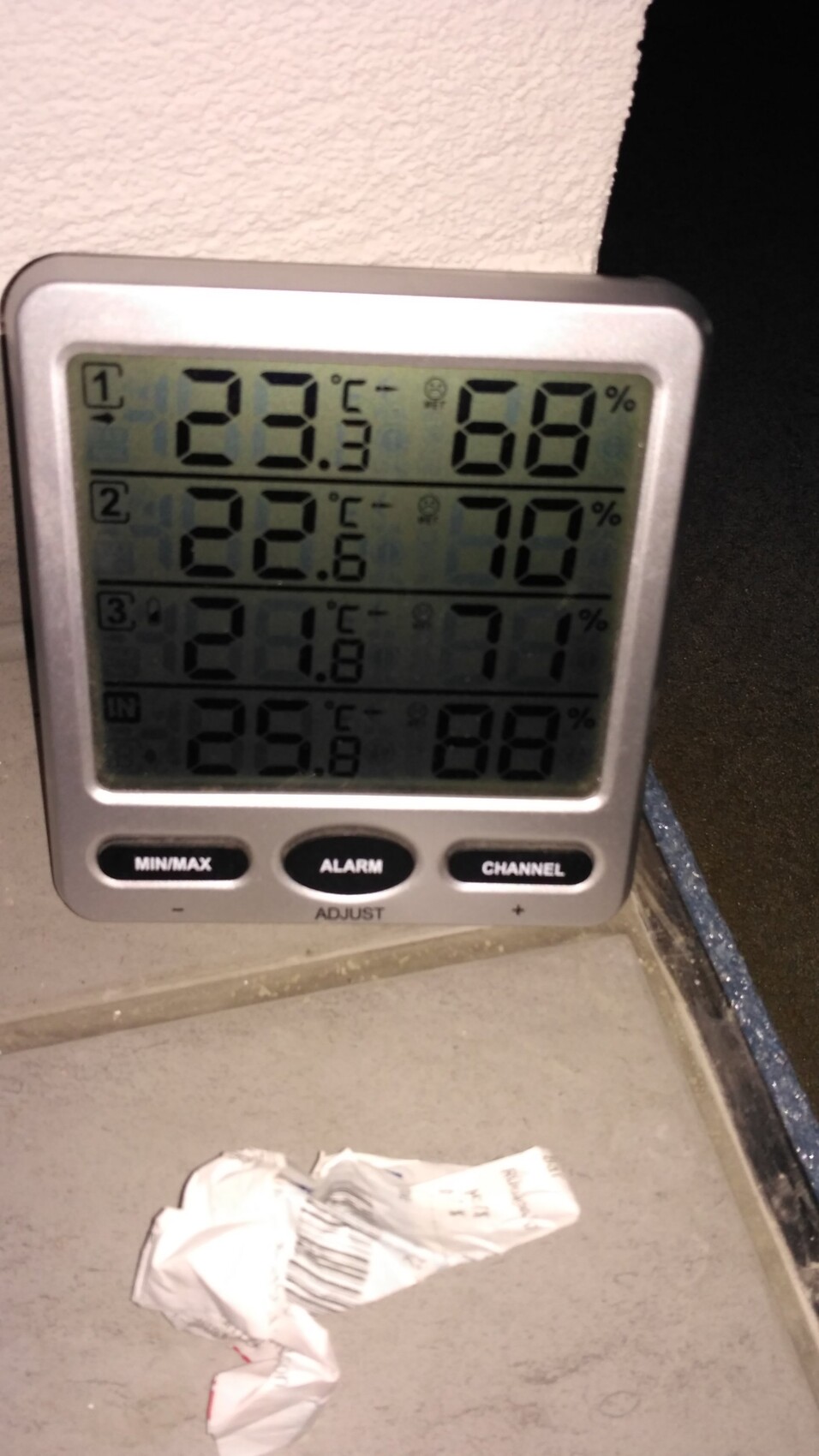Mehrkanal-Digitalthermometer zeigt Temperatur und Luftfeuchtigkeit, neben zerknittertem Zettel.