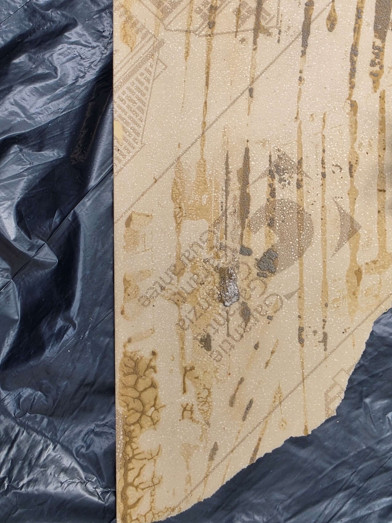 Karton mit braunen Tropfenflecken vor dunkler Plastikfolie.