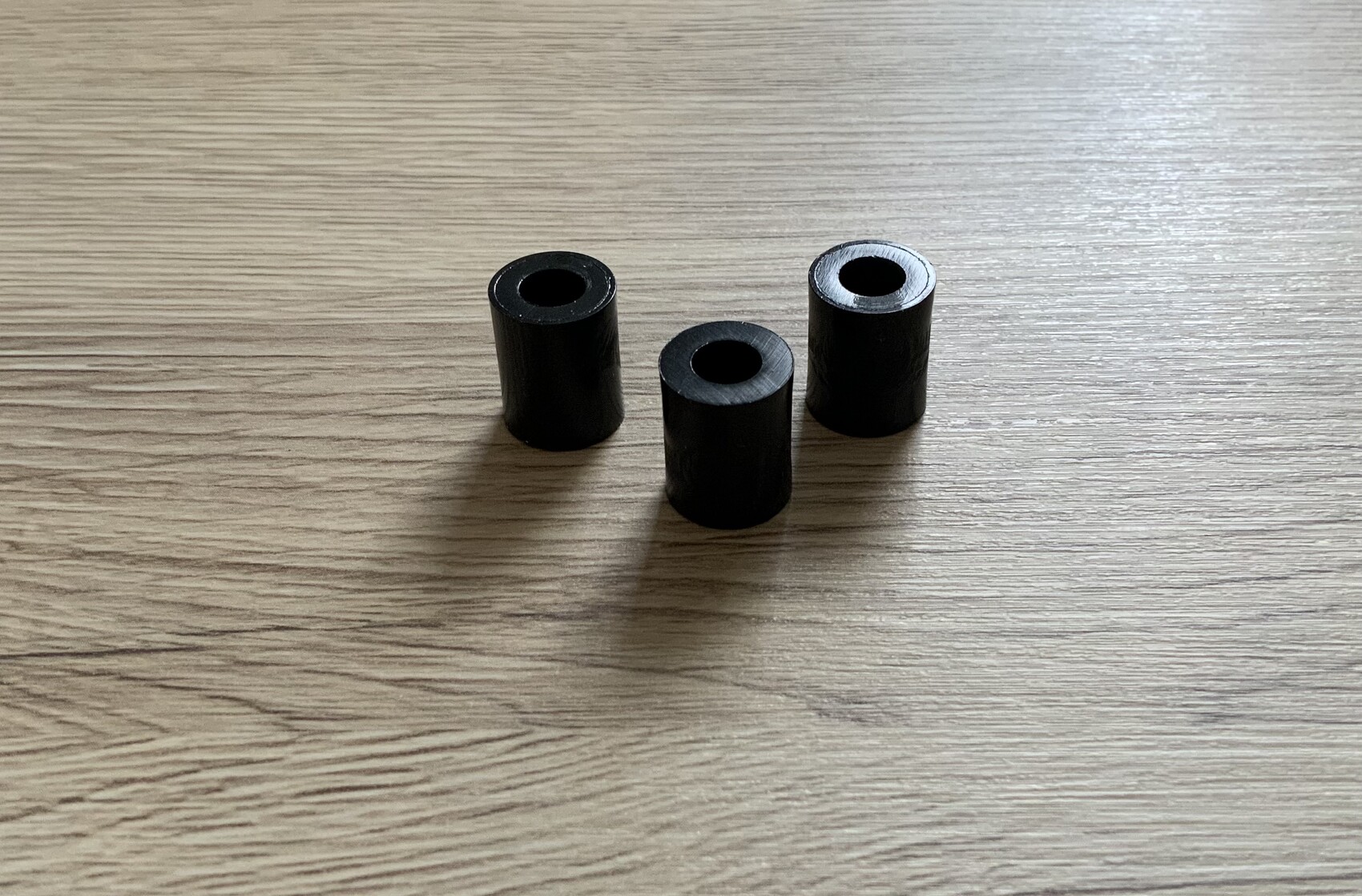 Drei schwarze, hohle Zylinder mit Loch in der Mitte auf einem Holztisch.