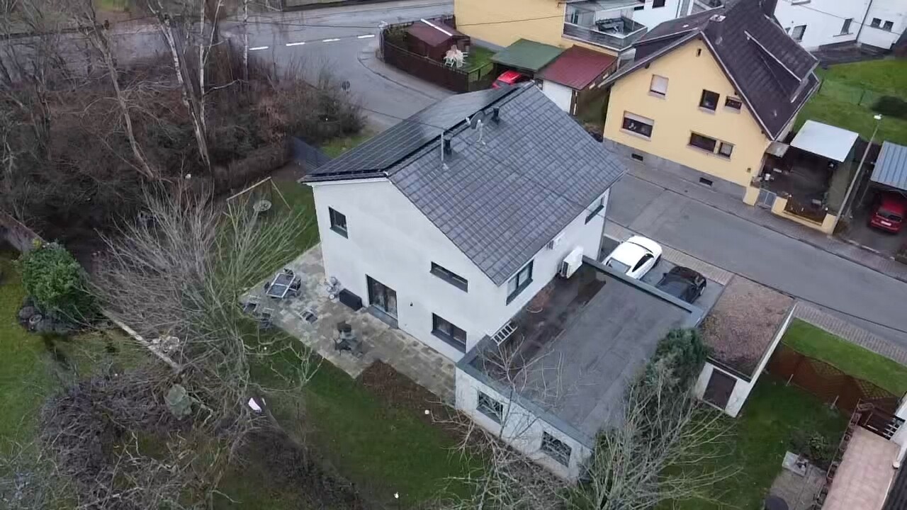 Vogelperspektive: Weißes zweistöckiges Haus mit grauem Dach, Parkplatz und Garten.