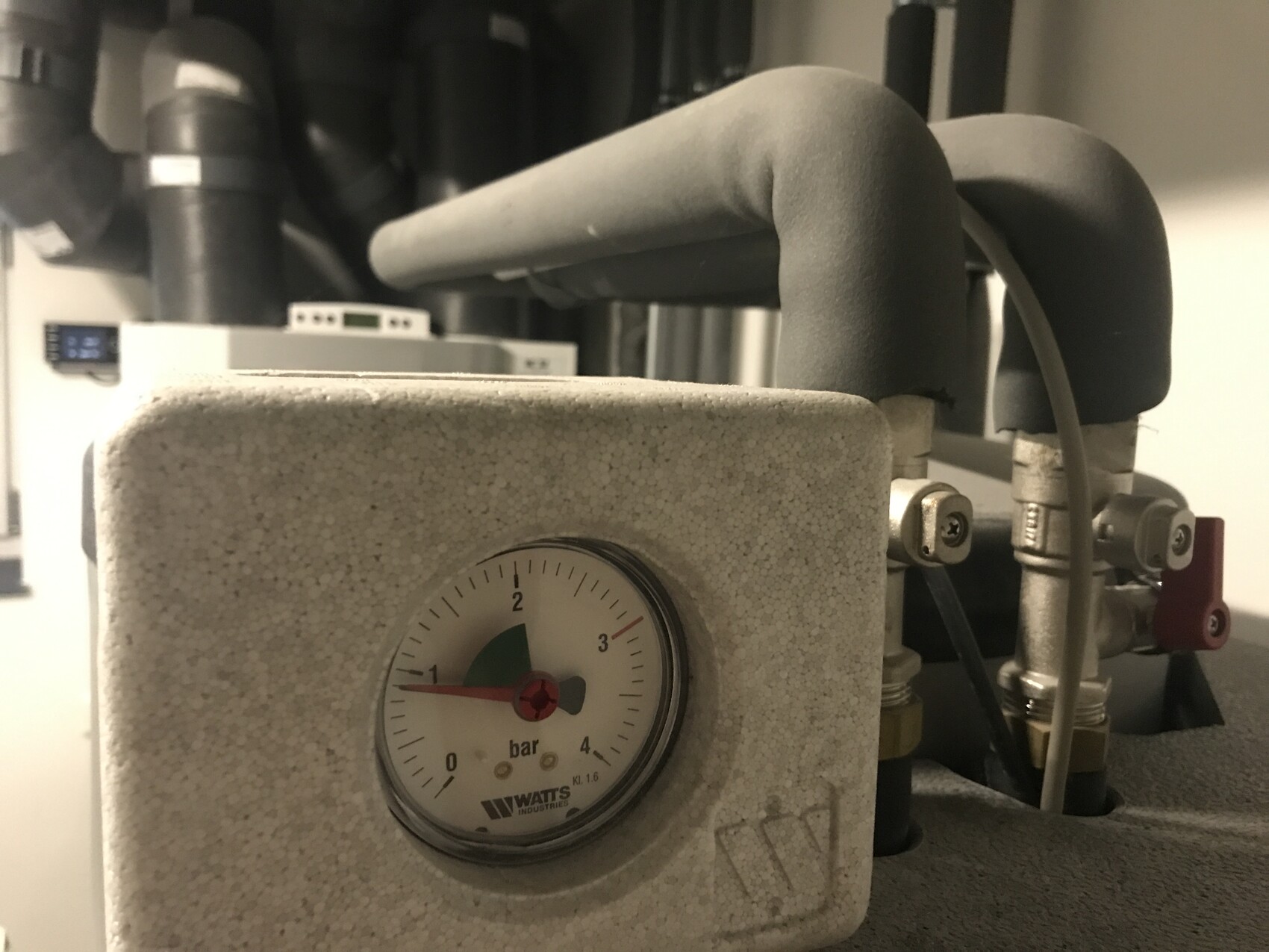 Druckmanometer in einer Industriemaschine, umgeben von Rohren, Ventilen und Isolierung.