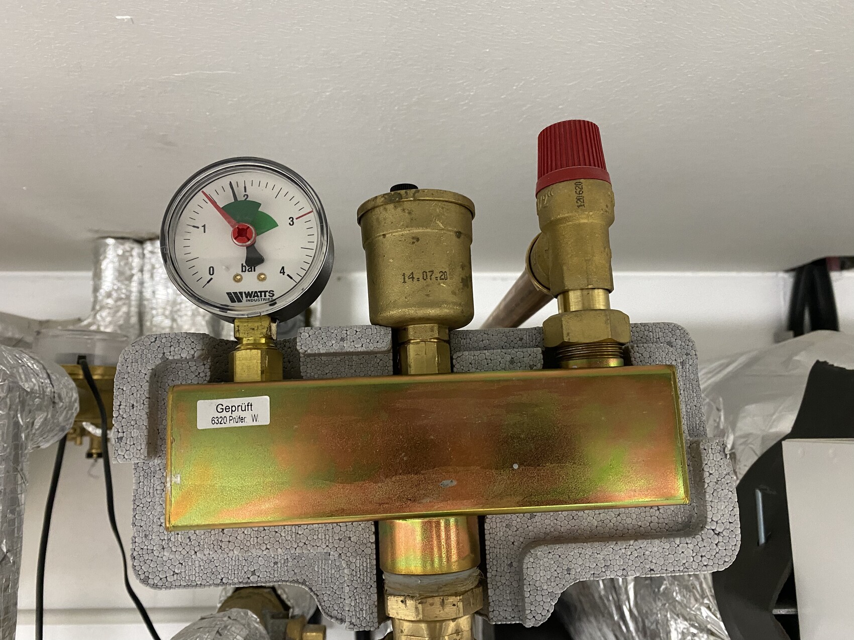 Druckmanometer (0-4 bar) an Heizungsrohr, roter Ventilknopf, Isolierung.