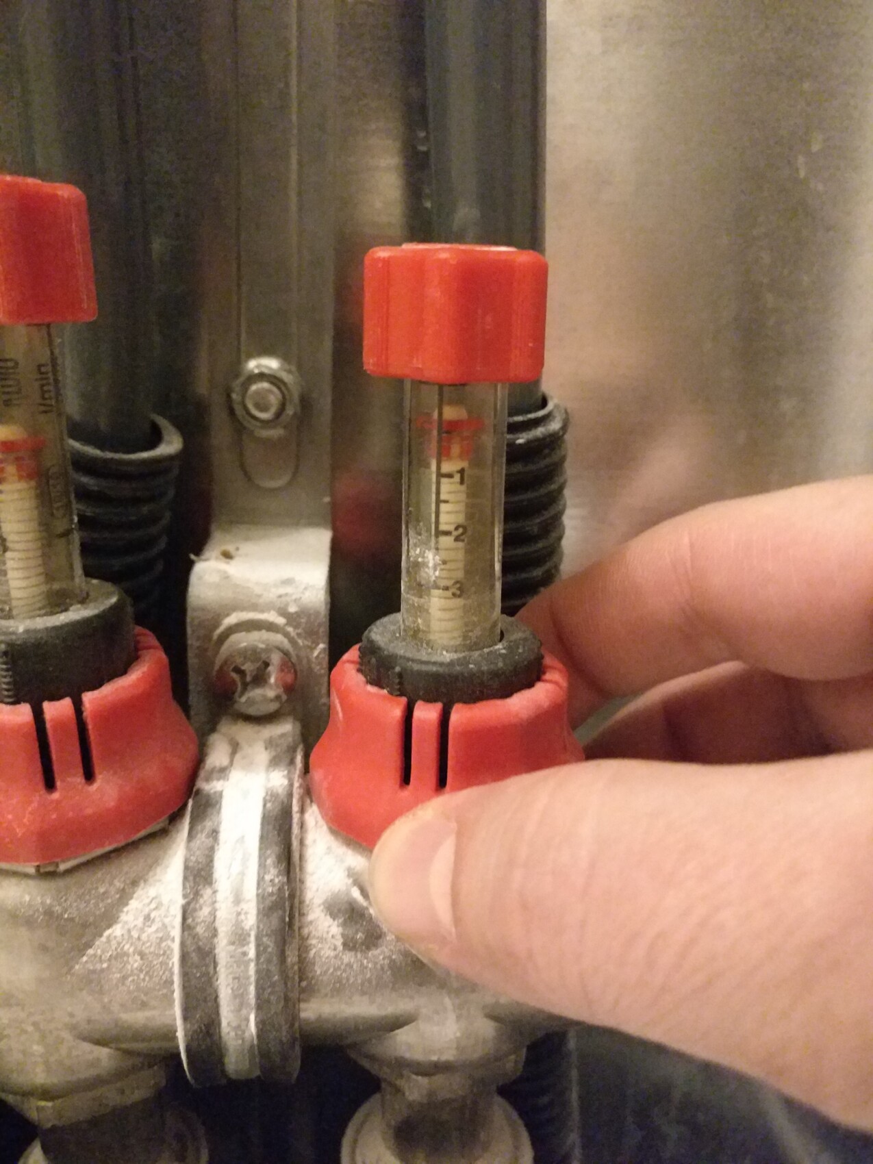 Nahaufnahme eines industriellen Ventils mit roter Kappe, Messskala und Hand, die es bedient.