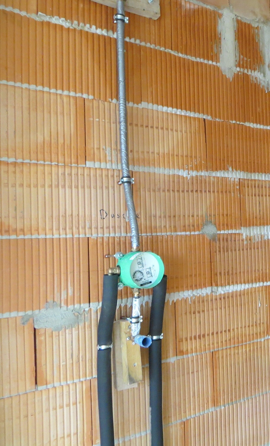Rohe Bauwand mit Wasserleitung, Rohrsystem und grünem Druckregler im Bauzustand