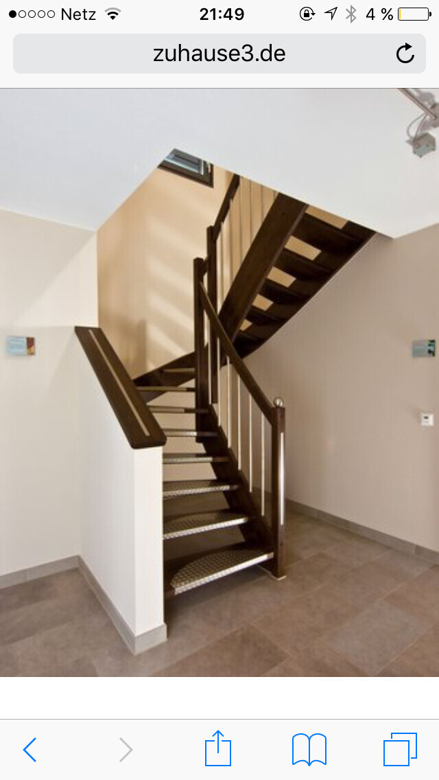 Moderne dunkle Holztreppe mit Geländer im hellen Treppenhaus und Fliesenboden.