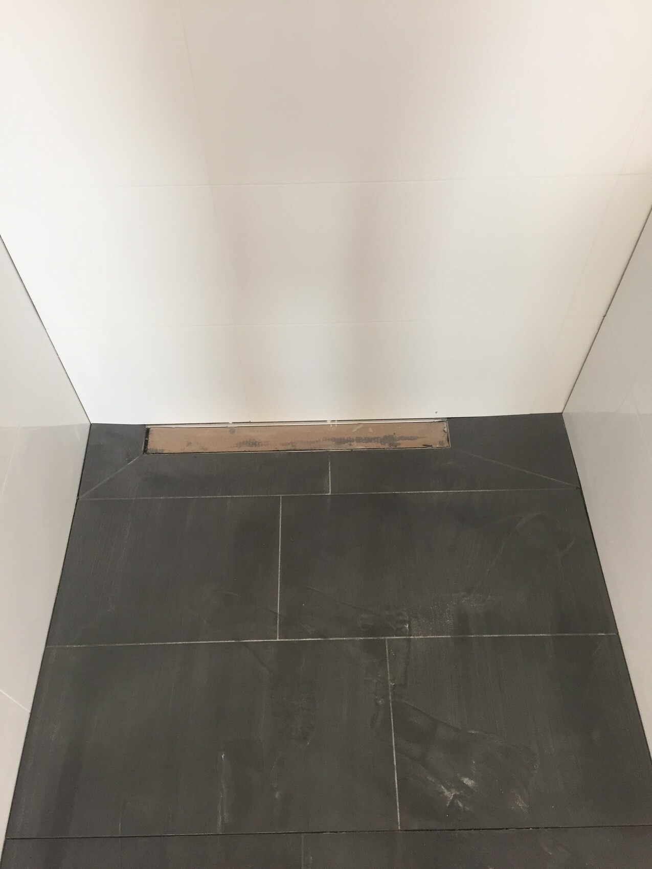 Badezimmer-Ecke: dunkle Bodenfliesen, weiße Wandfliesen, langer Bodenablauf an der Rückwand