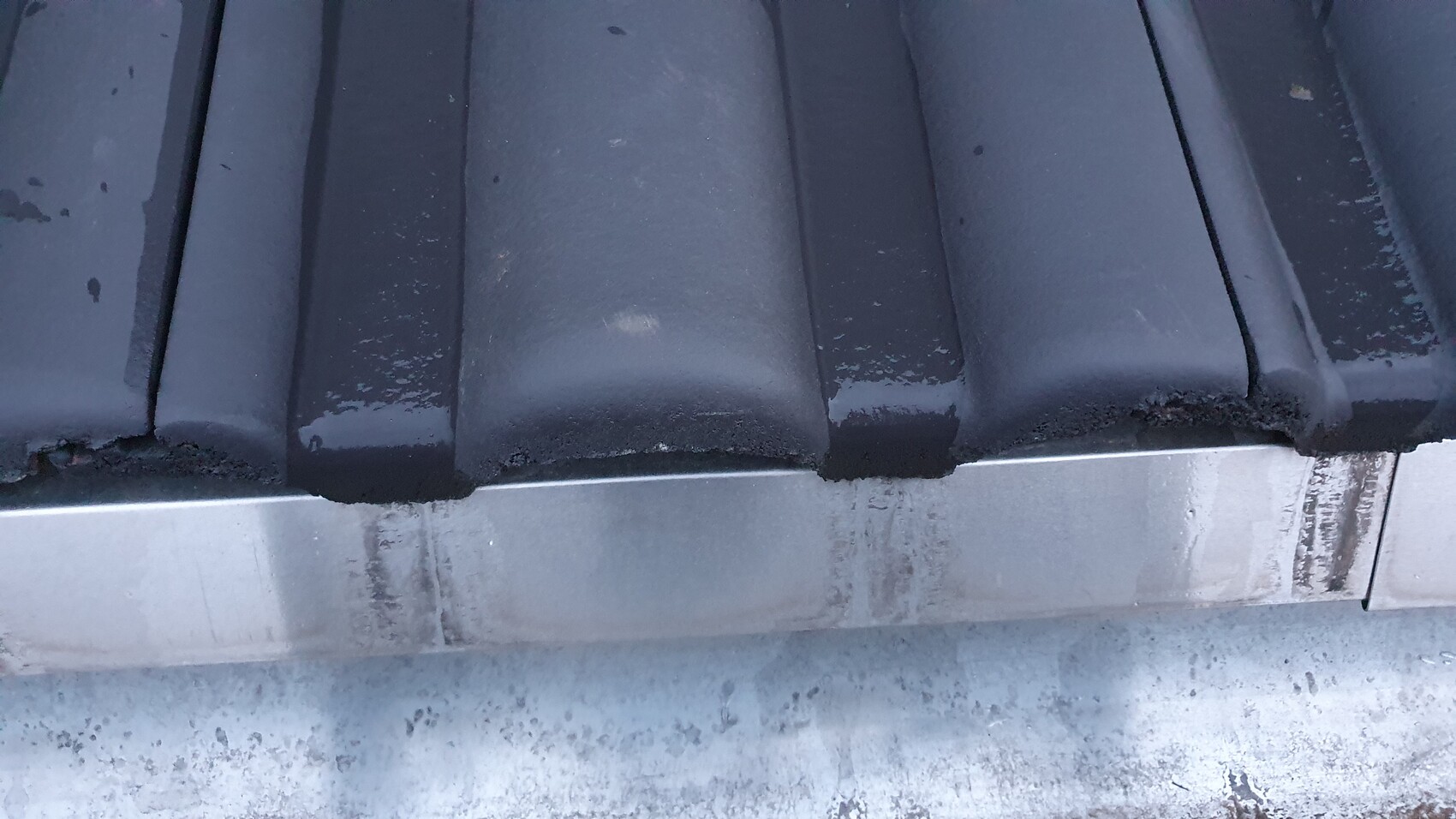 Nahaufnahme dunkelblauer Dachziegel mit Feuchtigkeit, darunter metallischer Rand.