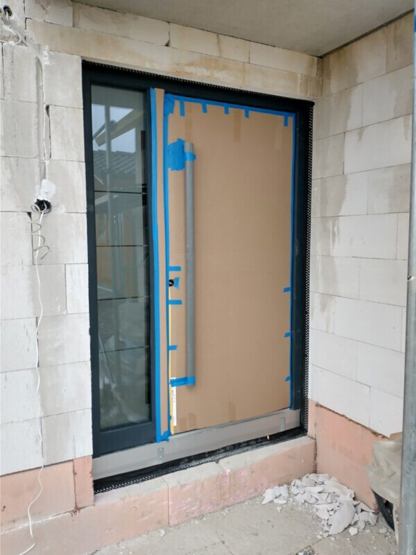 Tür mit Glasfront an Bauwand, Kartonabdeckung und blauem Malerband am Rahmen.