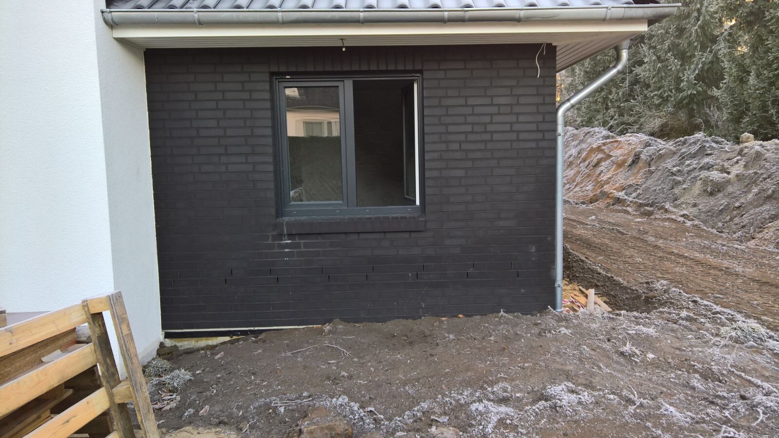 Außenansicht eines Hauses mit schwarzer Ziegelwand, Fenster und Baugrube.