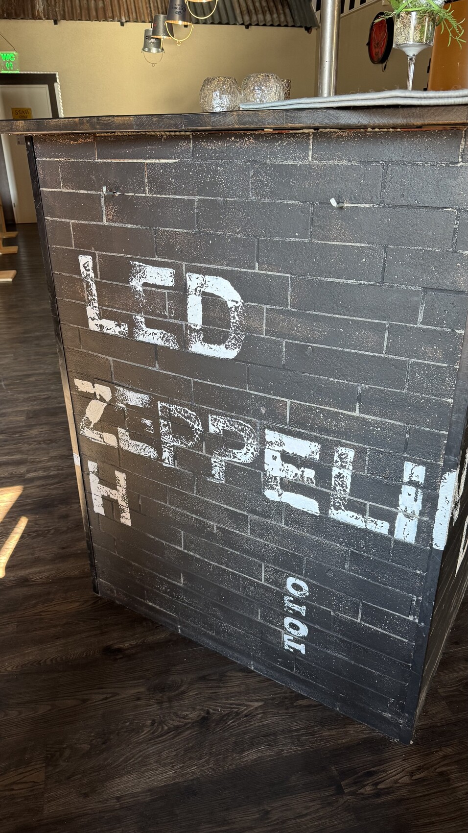 Dunkle Ziegelbarfront mit verwitterter weißer Stencil-Schrift, Innenraum im Hintergrund.