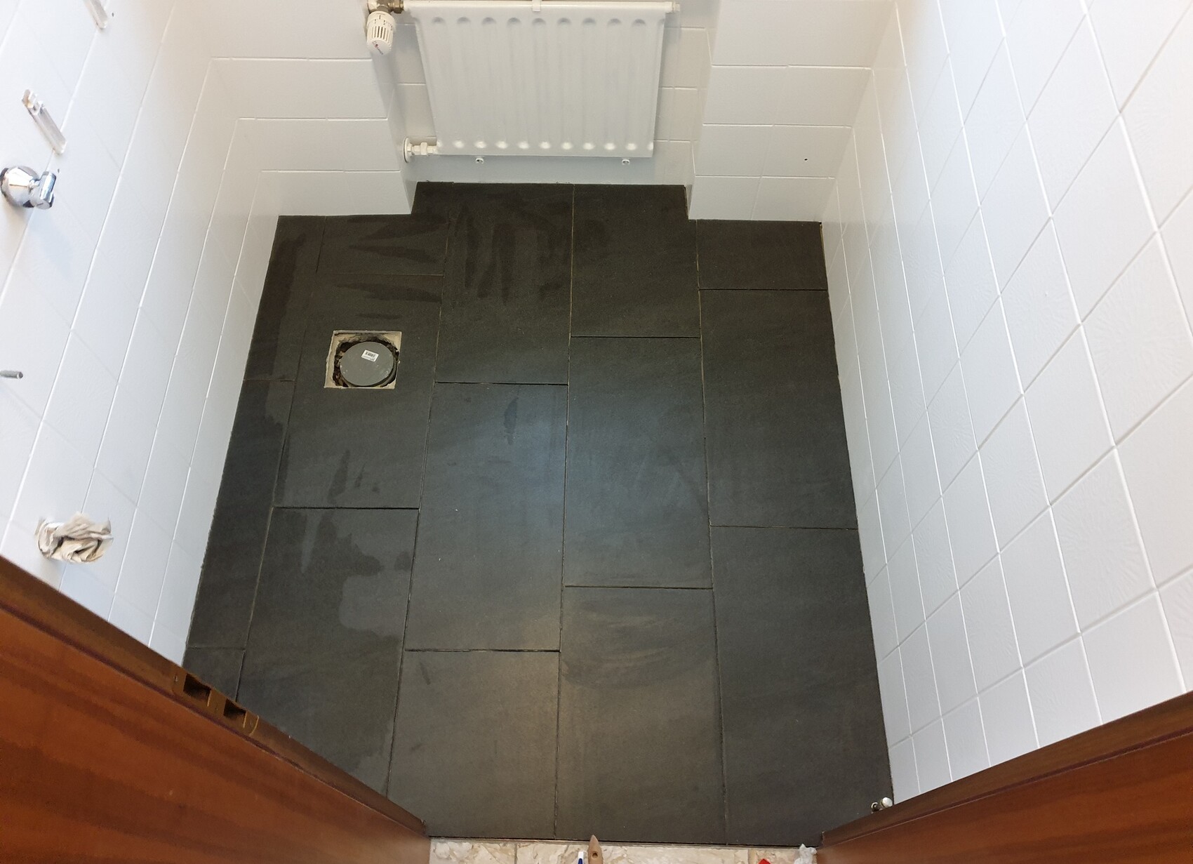 Kleines Badezimmer mit dunklem Fliesenboden, weißem Heizkörper und weißen Wandfliesen.