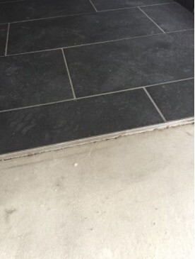 Dunkle rechteckige Bodenfliesen neben Betonstufe im Eingangsbereich