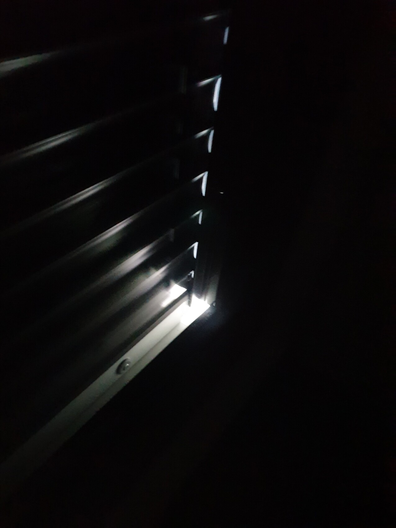 Dunkle Jalousie mit Lichtstreifen, der durch die Lamellen fällt.
