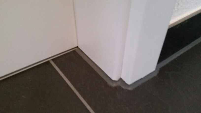 Weiße Türrahmenkante trifft dunkle Fliesen am Boden, Ecke zwischen Wand und Türöffnung.