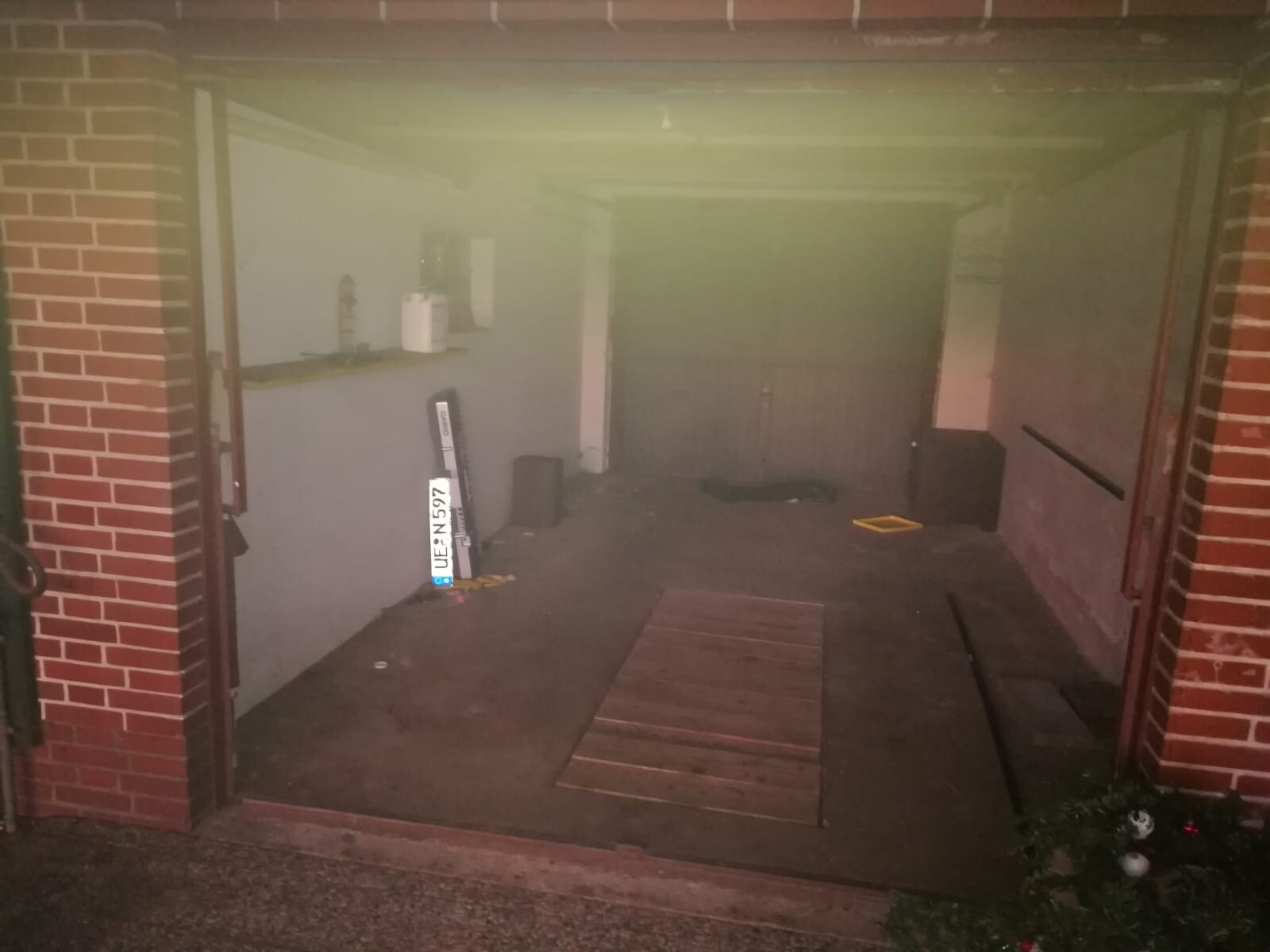Offene Garage mit Holzbodenplatten, links Regal mit Gegenständen, gelbe Ablagefläche.