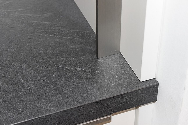 Dunkle Granit-Arbeitsplatte mit rechteckigem Metallbein vor weißer Wand.
