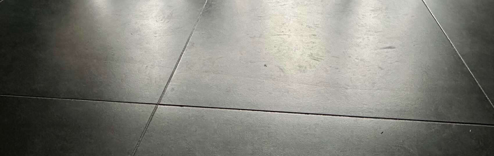 Dunkle graue Bodenfliesen mit diagonalen Fugenlinien und glatter Oberfläche.