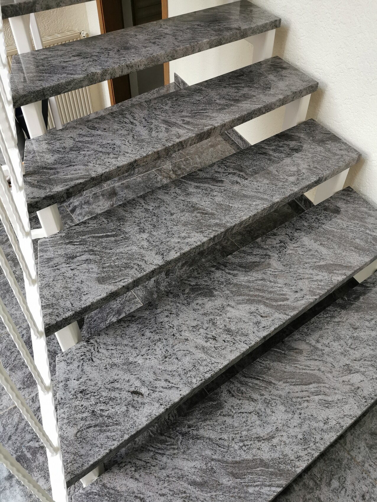 Moderne Treppe aus grauem Granit mit offenen Stufen an weißer Wand