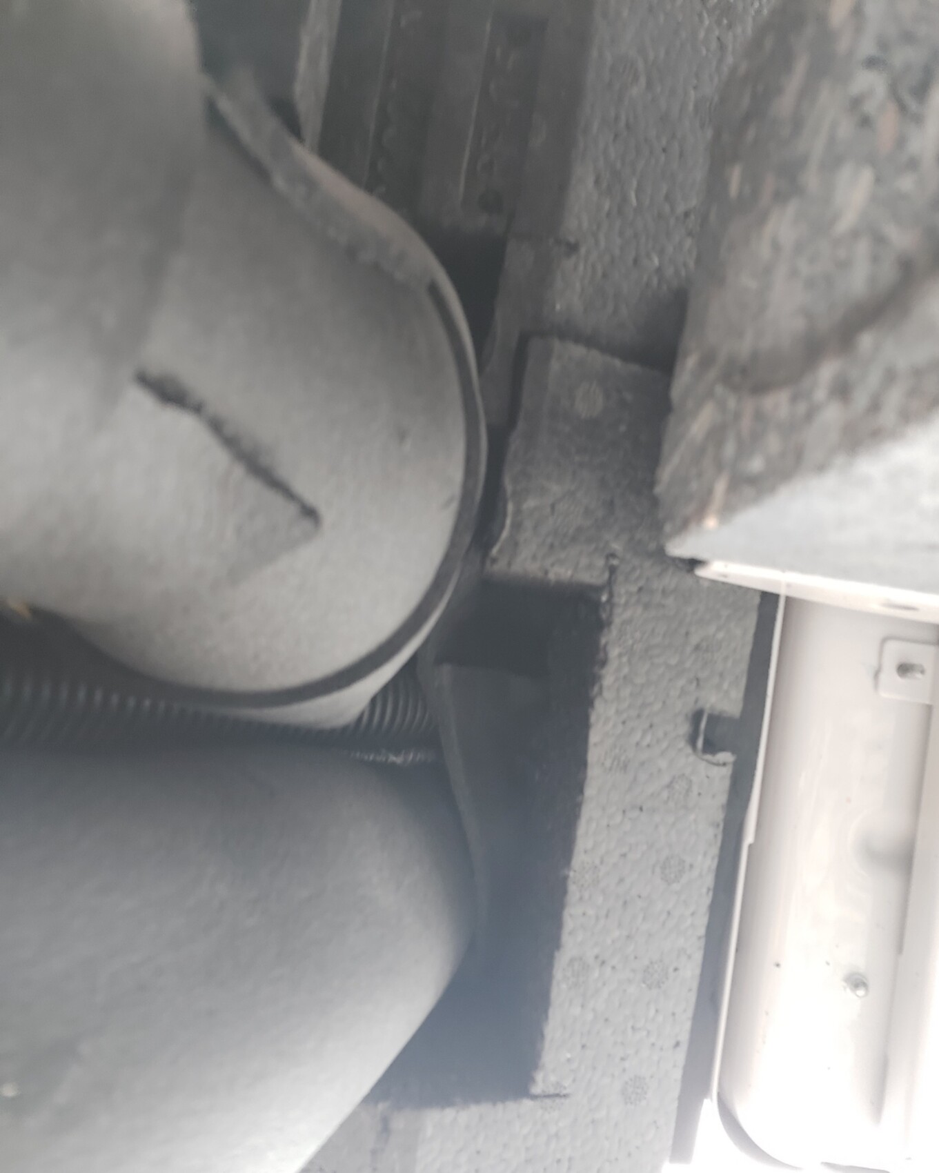Unterboden eines Autos nahe dem Radkasten, staubige Bauteile und Schläuche sichtbar.