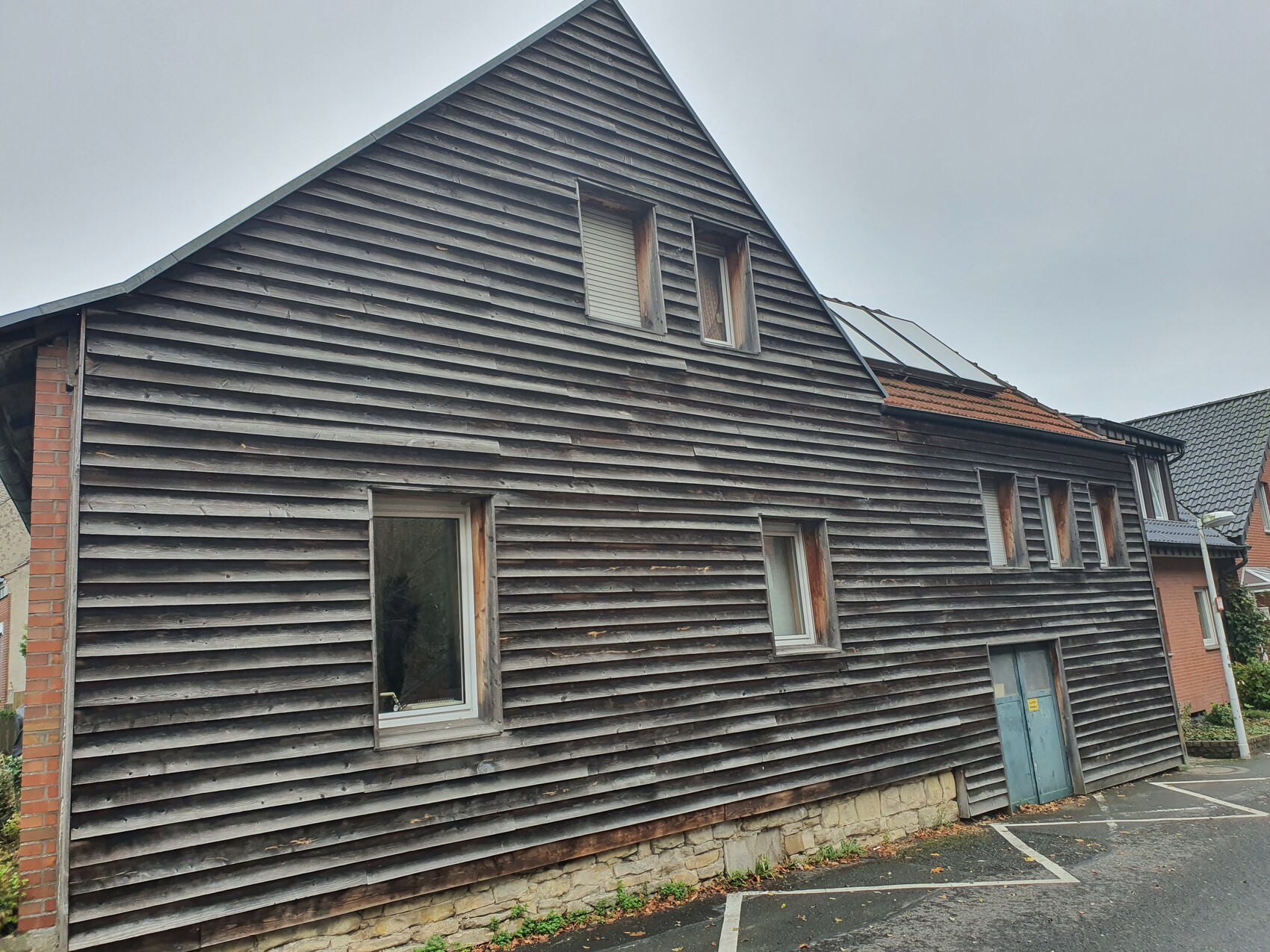Holzhaus mit schrägem Giebel, horizontaler Verkleidung, mehreren Fenstern und blauer Tür.