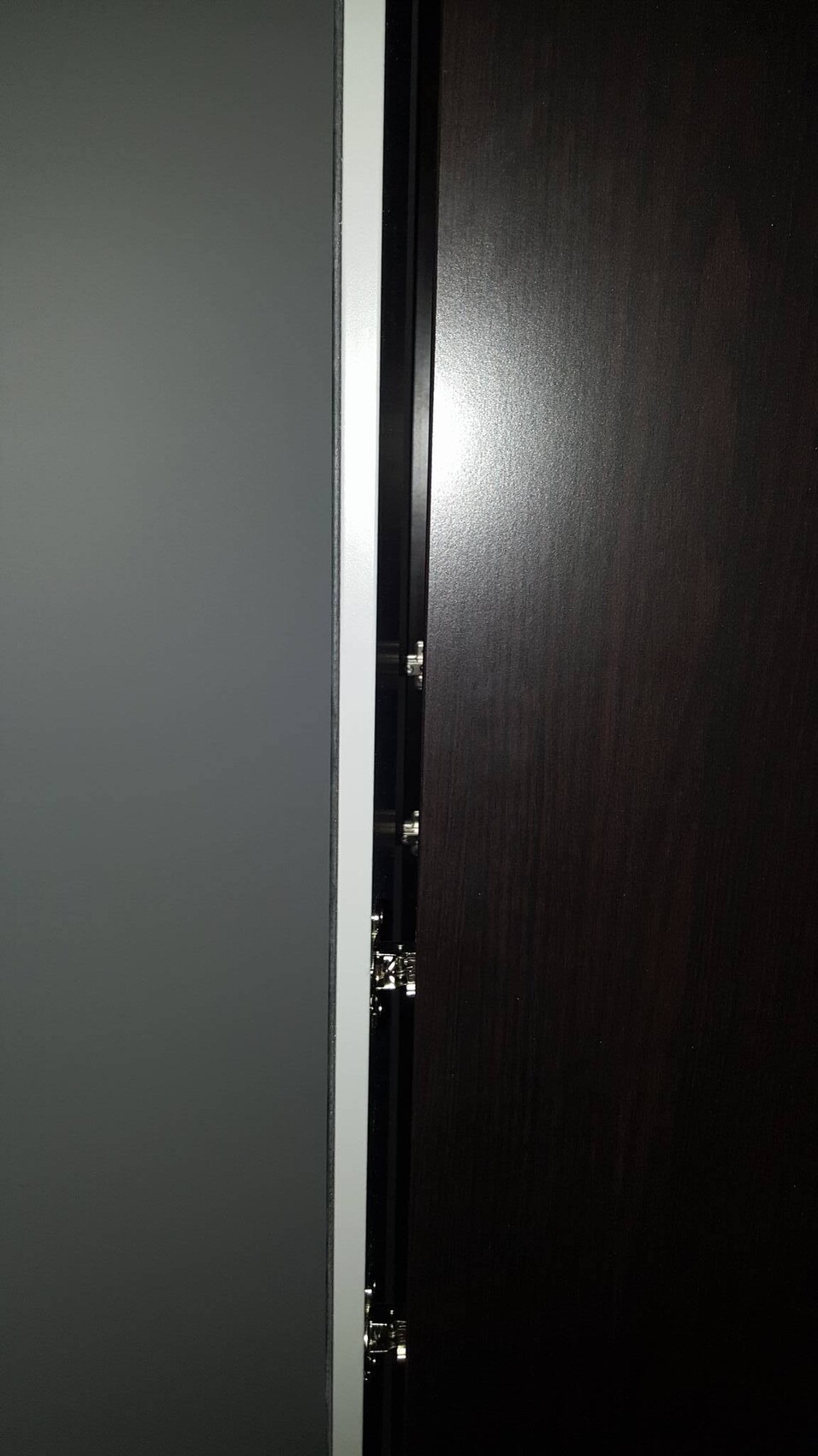 Nahaufnahme einer dunklen Holztür mit sichtbaren Metallscharniere an der Türkante.