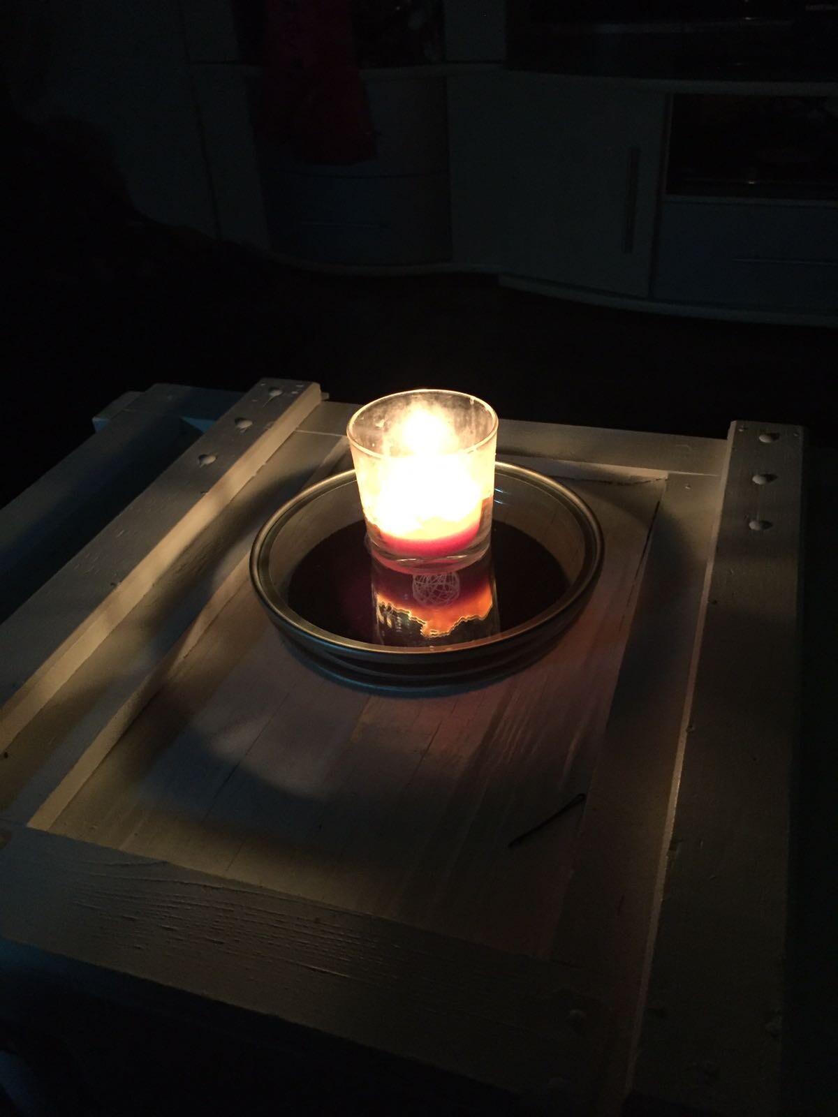 Dunkle Küche mit brennender Kerze in Glas auf Teller auf Holztisch vor Küchenzeile.
