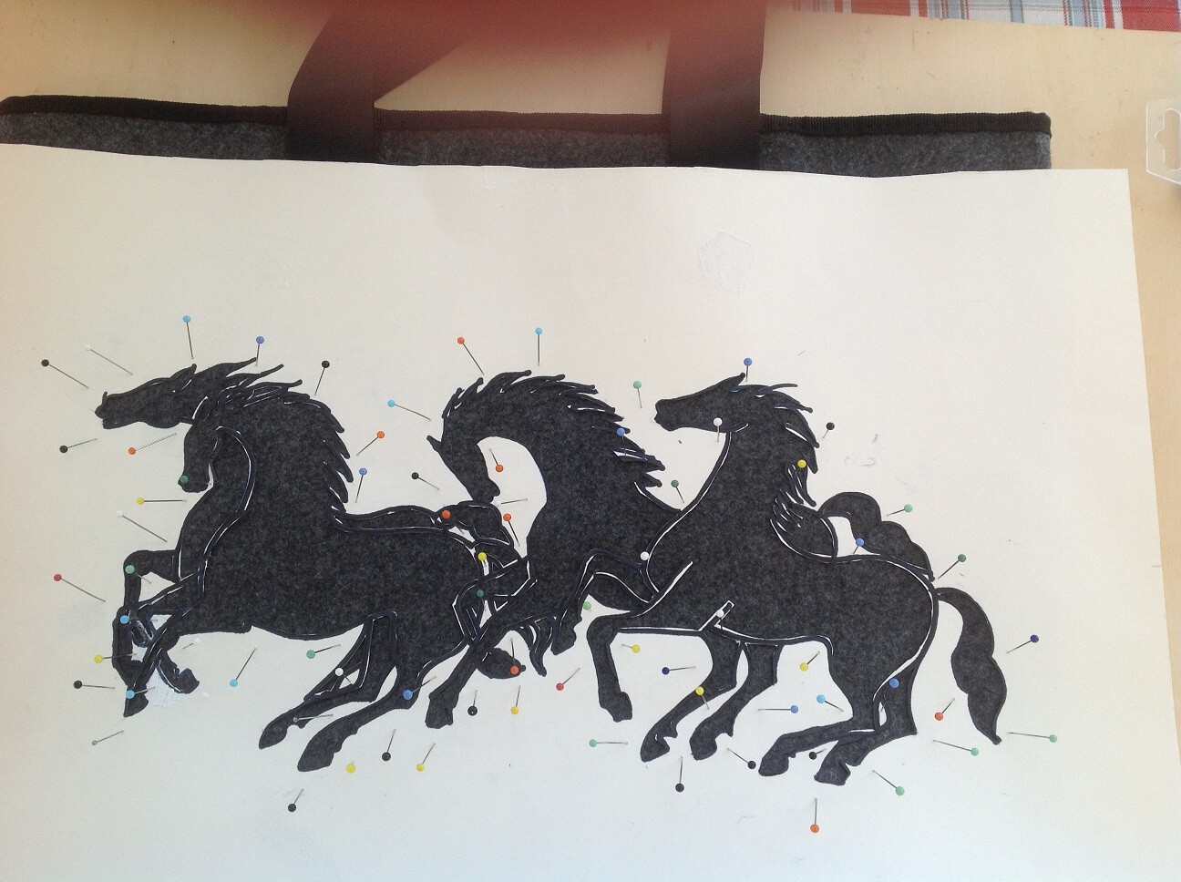 Drei schwarze Pferde im Galopp, umgeben von bunten Stecknadeln.