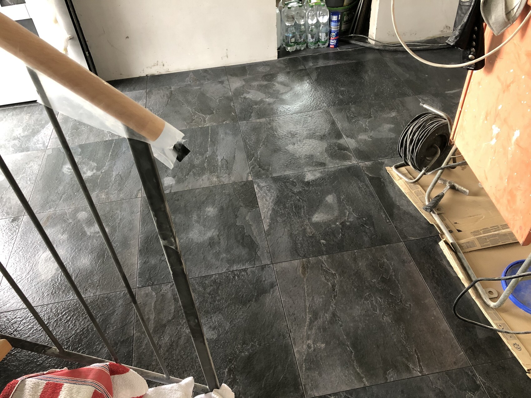Dunkler Fliesenboden in Renovierungsraum; Kabelrolle auf Karton, Bauwerkzeuge im Hintergrund.