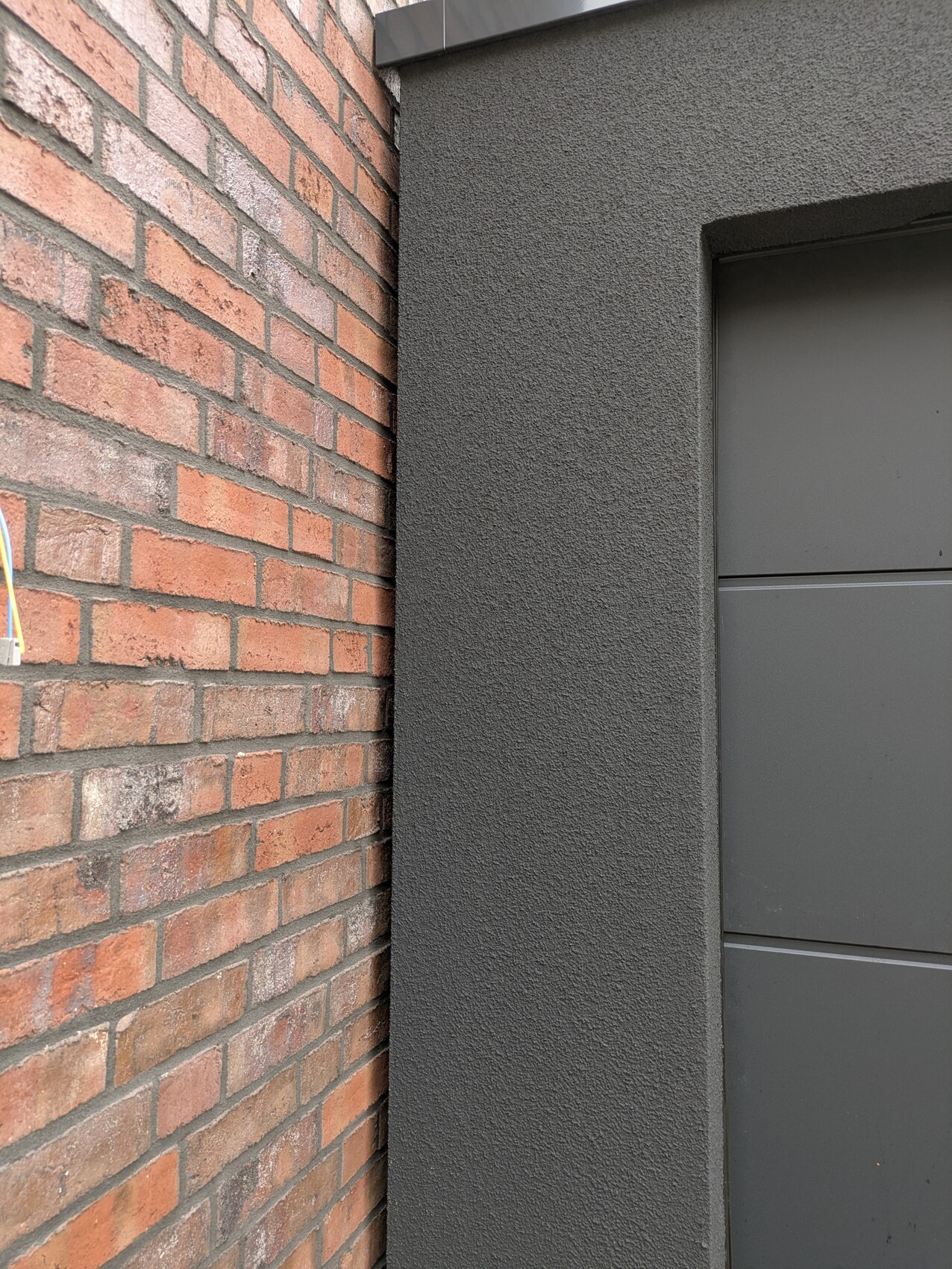 Außenansicht: dunkle Türfront neben roter Backsteinwand