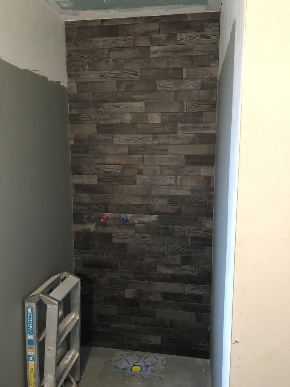 Kleines Bad mit dunkler Holzfliesen-Wand, rote und blaue Wasseranschlüsse, Leiter links.