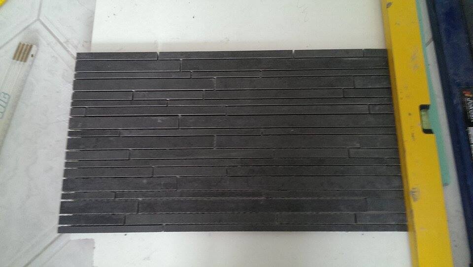 Probe dunkler, schmaler Wandfliesen auf weißer Arbeitsfläche mit gelber Wasserwaage.