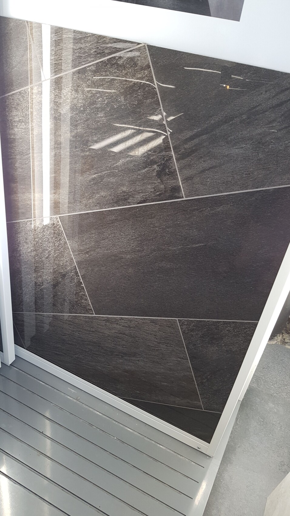 Außenbereich mit dunklen Wandfliesen und grauem Terrassenboden neben Glasrahmen