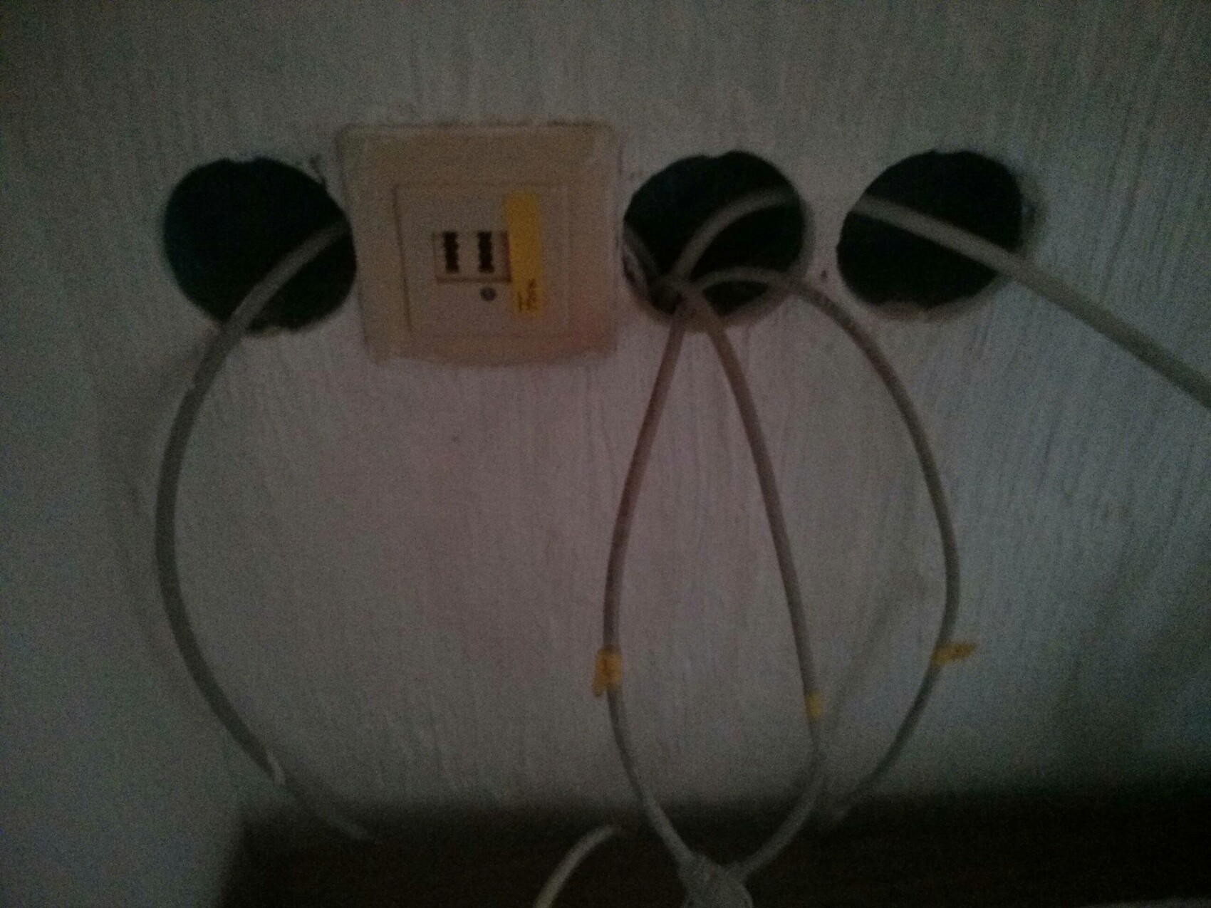 Dunkle Wandinstallation mit drei runden Öffnungen, Steckdose und Kabeln