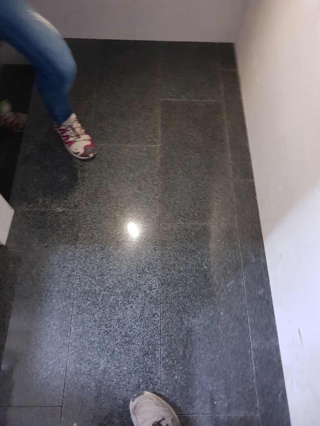 Person steht auf dunklen Fliesenboden in Innenraum, Nahaufnahme der grauen Bodenbeläge.