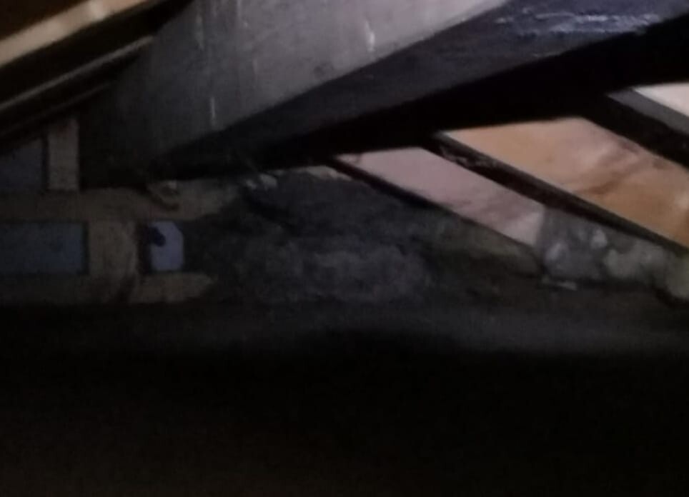 Dunkler Dachboden mit Holzbalken, Dämmung und staubigem Boden; wenig Licht.