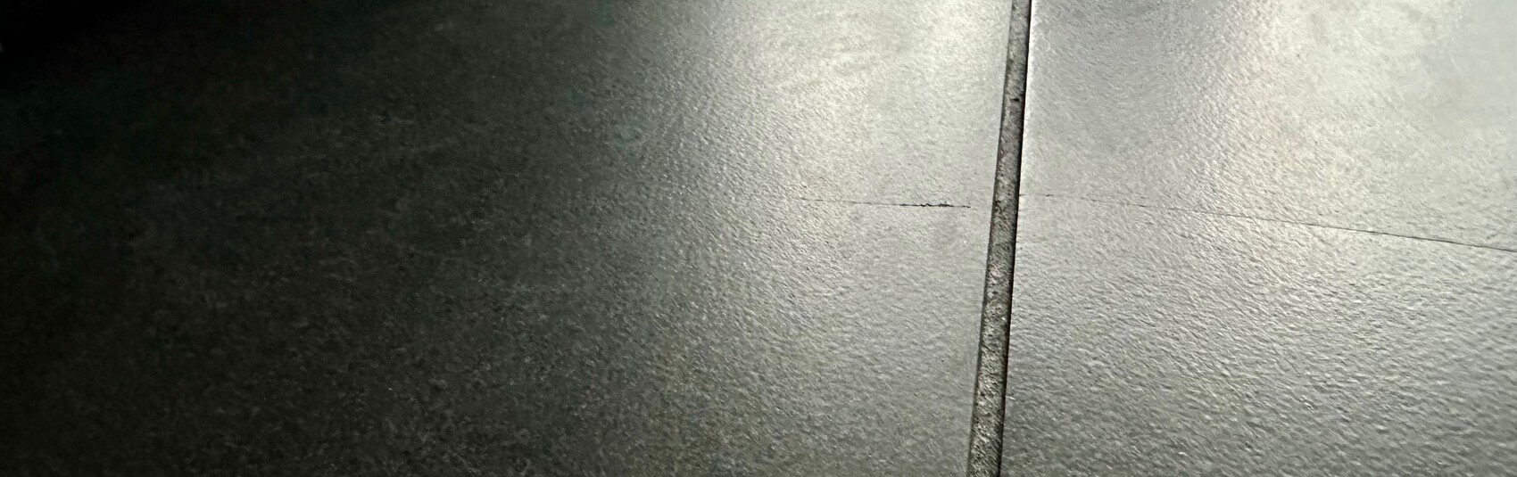 Nahaufnahme einer dunklen grauen Fliesenoberfläche mit senkrechter Fuge und horizontaler Linie.