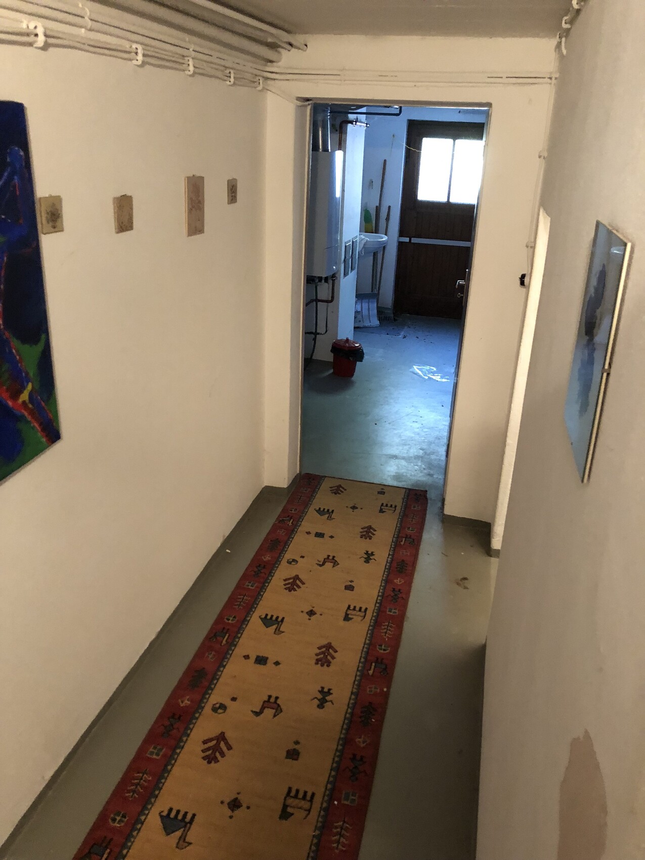 Langer Kellerflur mit beigem Teppichläufer, Wandbildern und Tür am Ende zum Waschkeller.