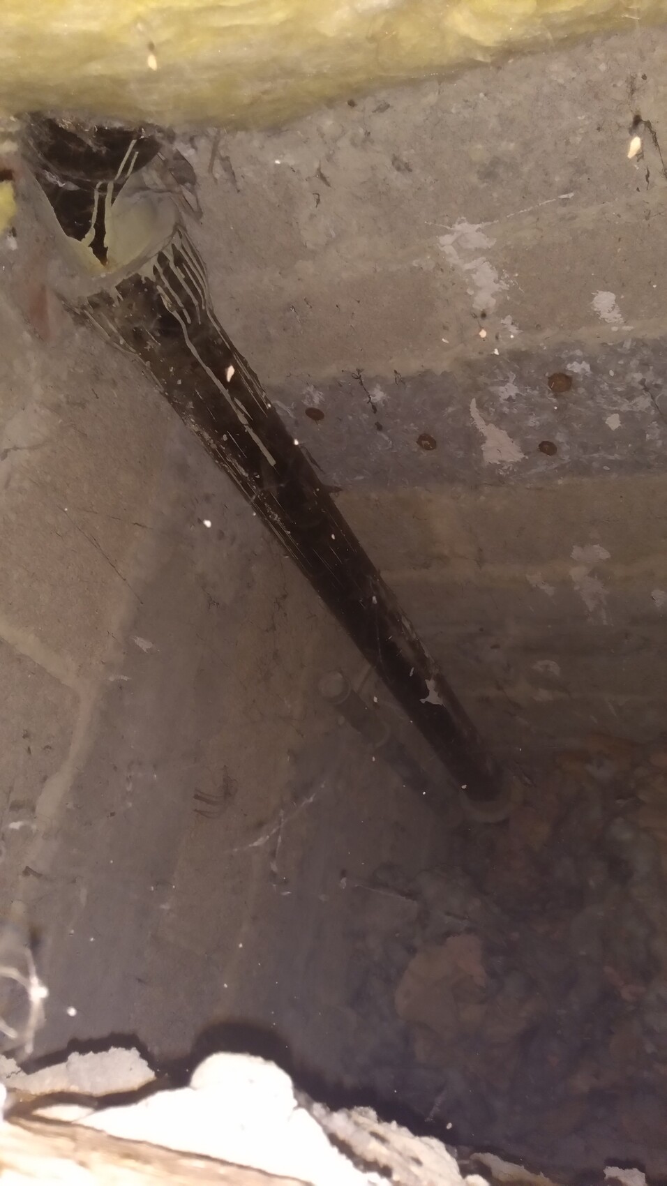 Schwarzes Rohr verläuft schräg durch staubigen Betonbau, Gelber Dämmstoff oben.