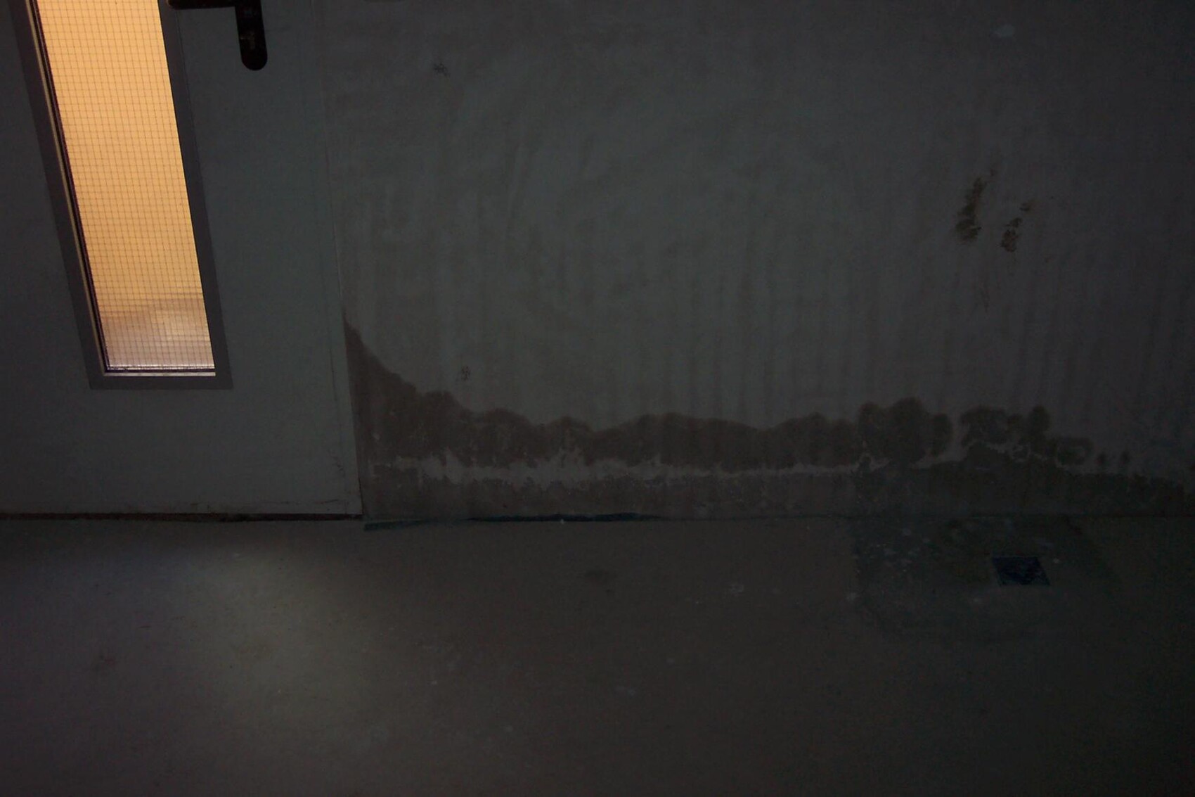 Dunkler Kellerraum mit Feuchtigkeit an der Wand und kleinem Fenster links