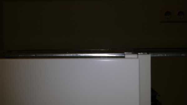 Dunkler Raum mit einer weißen Küchenschrank-Tür und einer Metallkante/Schiene oben.