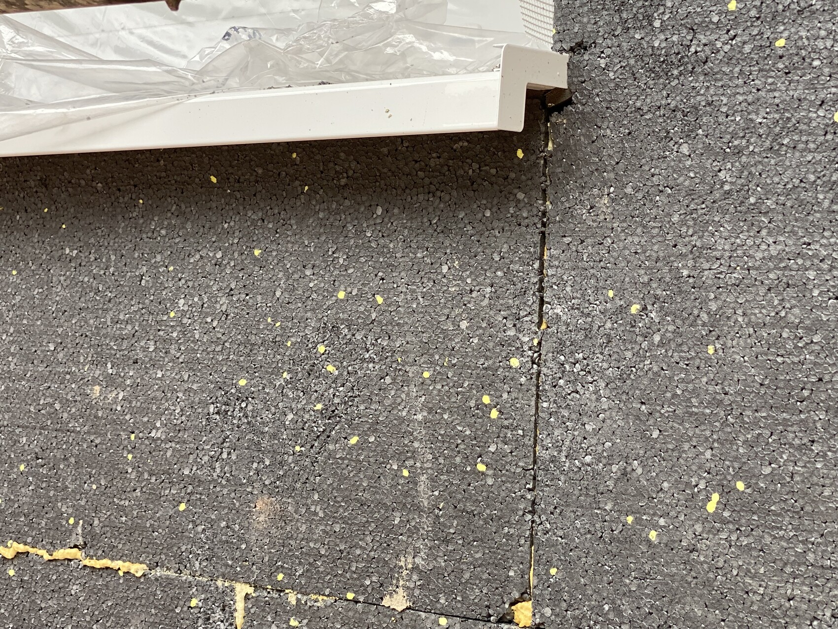 Nahaufnahme schwarzer Dachschindeln mit gelben Flecken und einer weißen Randleiste.
