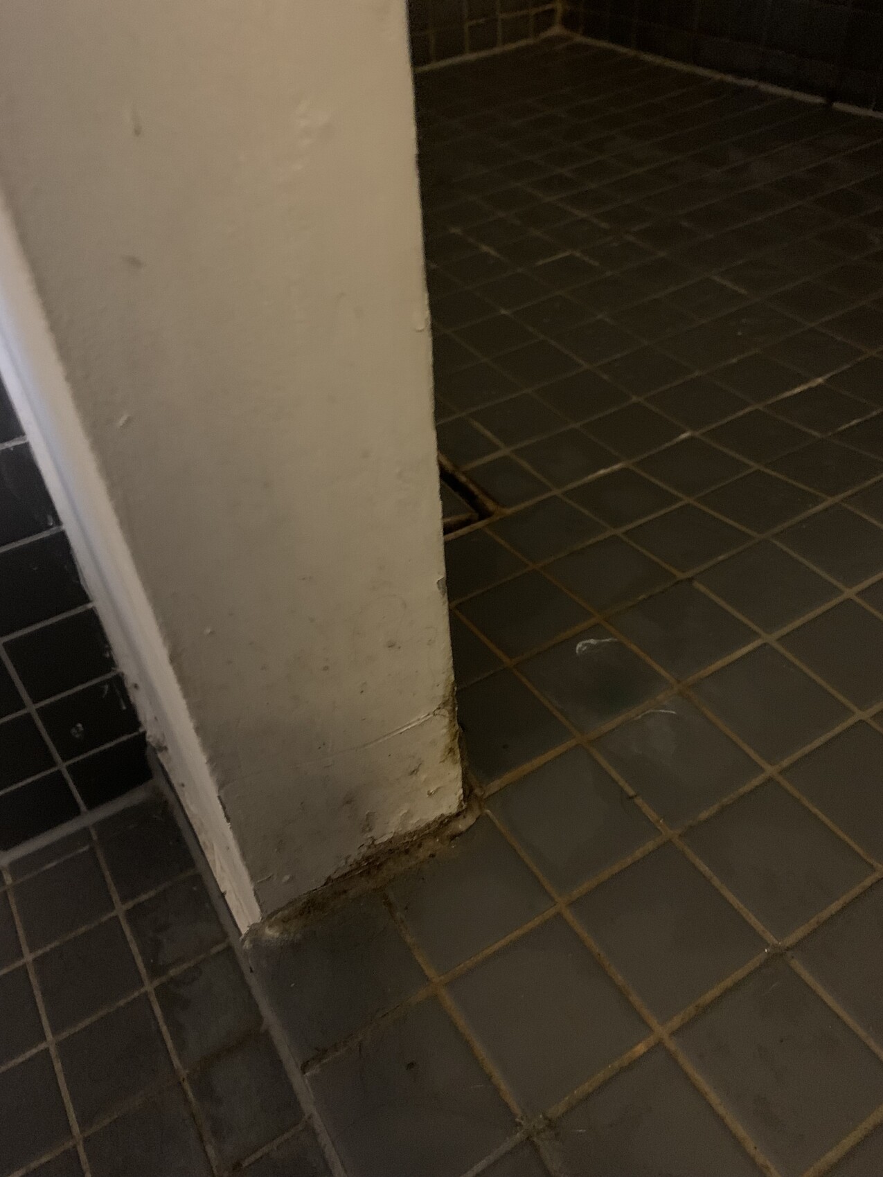 Weiße Wandsäule neben grauen Fliesen, Bodenrand verschmutzt.