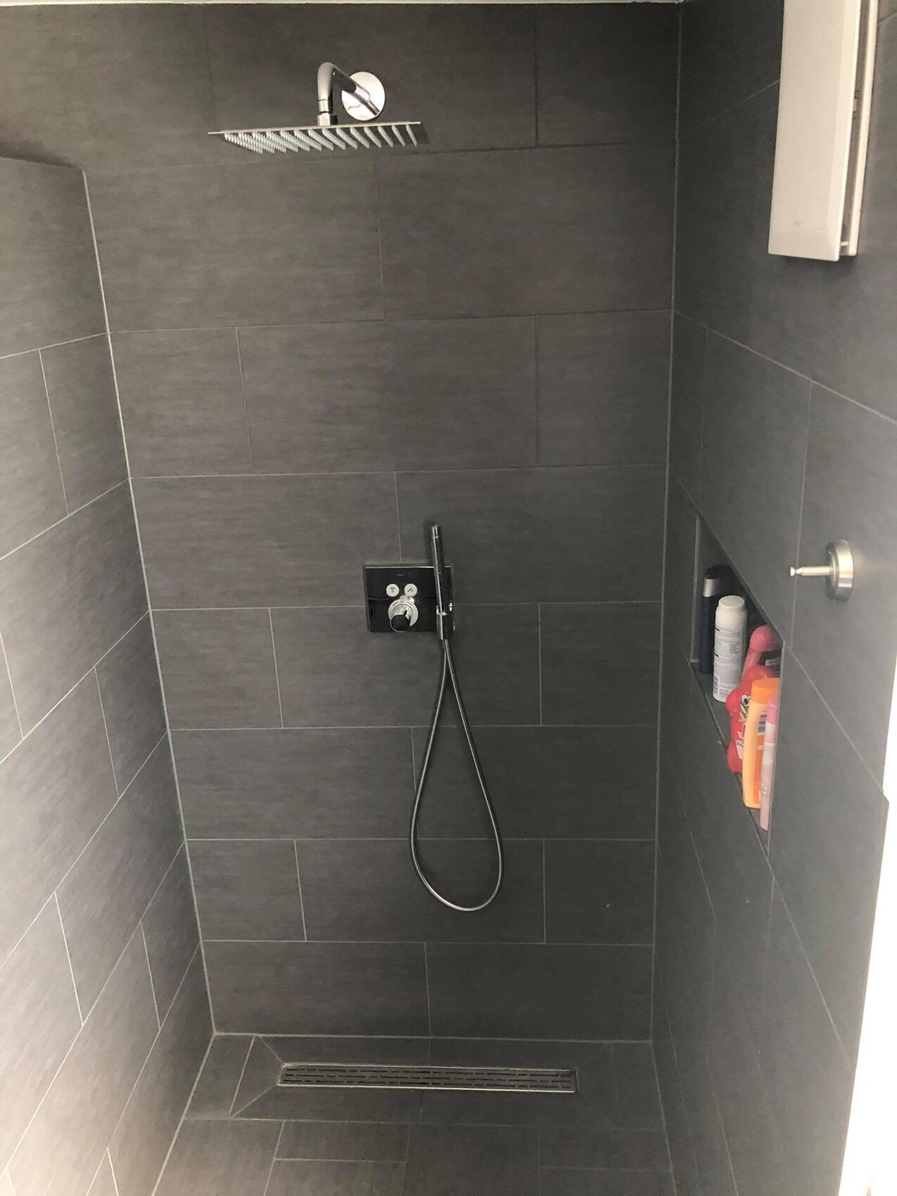 Dunkelgraue Dusche mit Decken-Regenkopf, Handbrause an der Wand und Nische mit Pflegeprodukten.