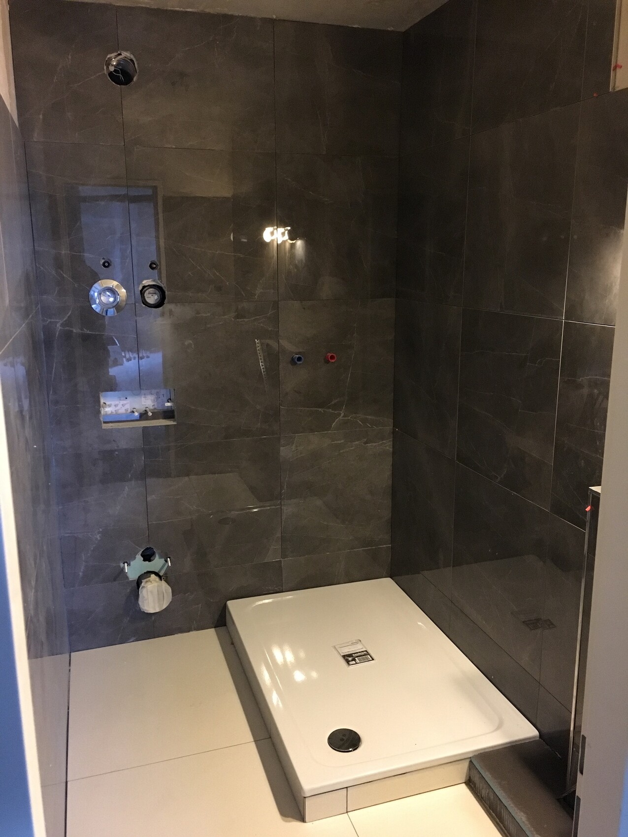Moderne Dusche mit dunkelgrauen Fliesen, weißer quadratischer Duschwanne und Armaturen.
