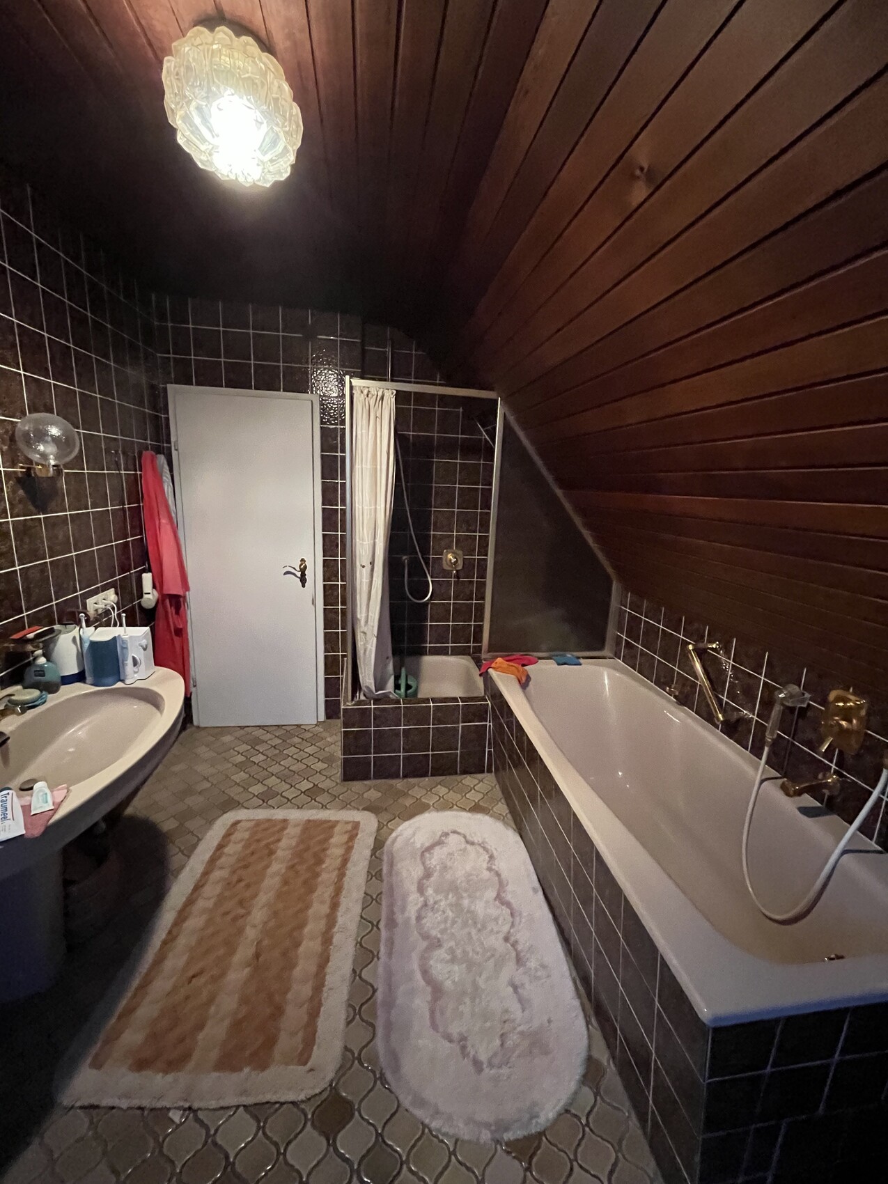 Dachgeschoss-Badezimmer mit dunklen Fliesen, Badewanne, Dusche, Waschbecken und zwei Matten