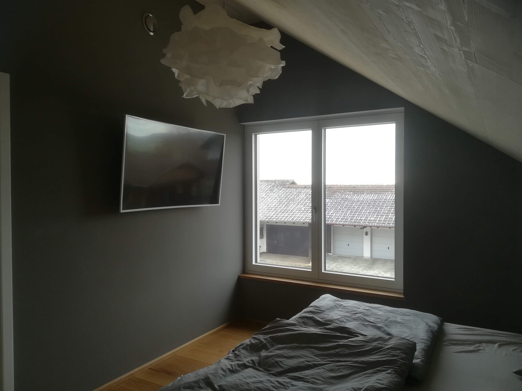 Schlafzimmer mit dunklen Wänden, Bett und TV, großes Fenster mit Garagenblick.