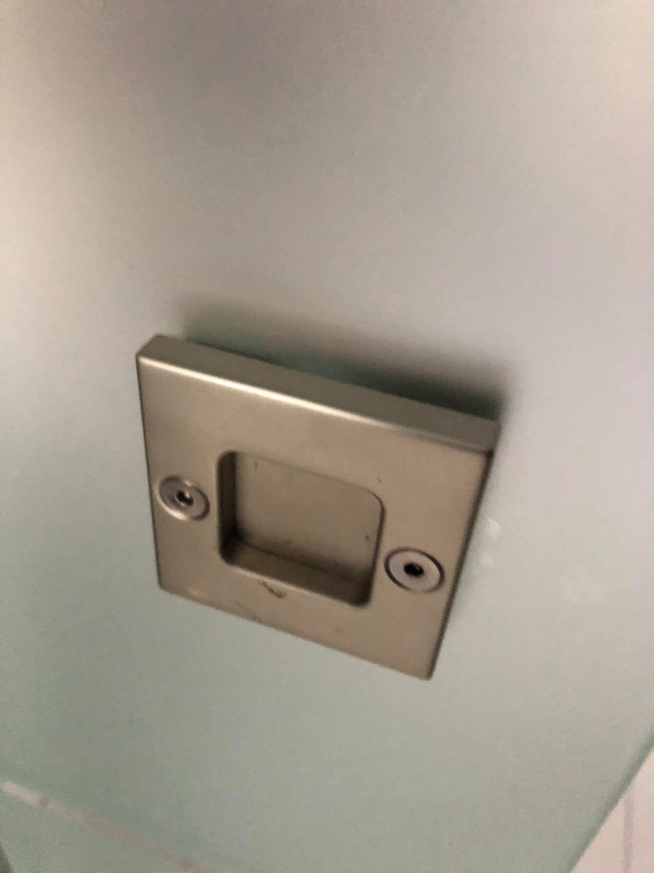 Flacher, quadratischer Metallgriff mit eingelassener Mulde an einer hellblauen Tür.
