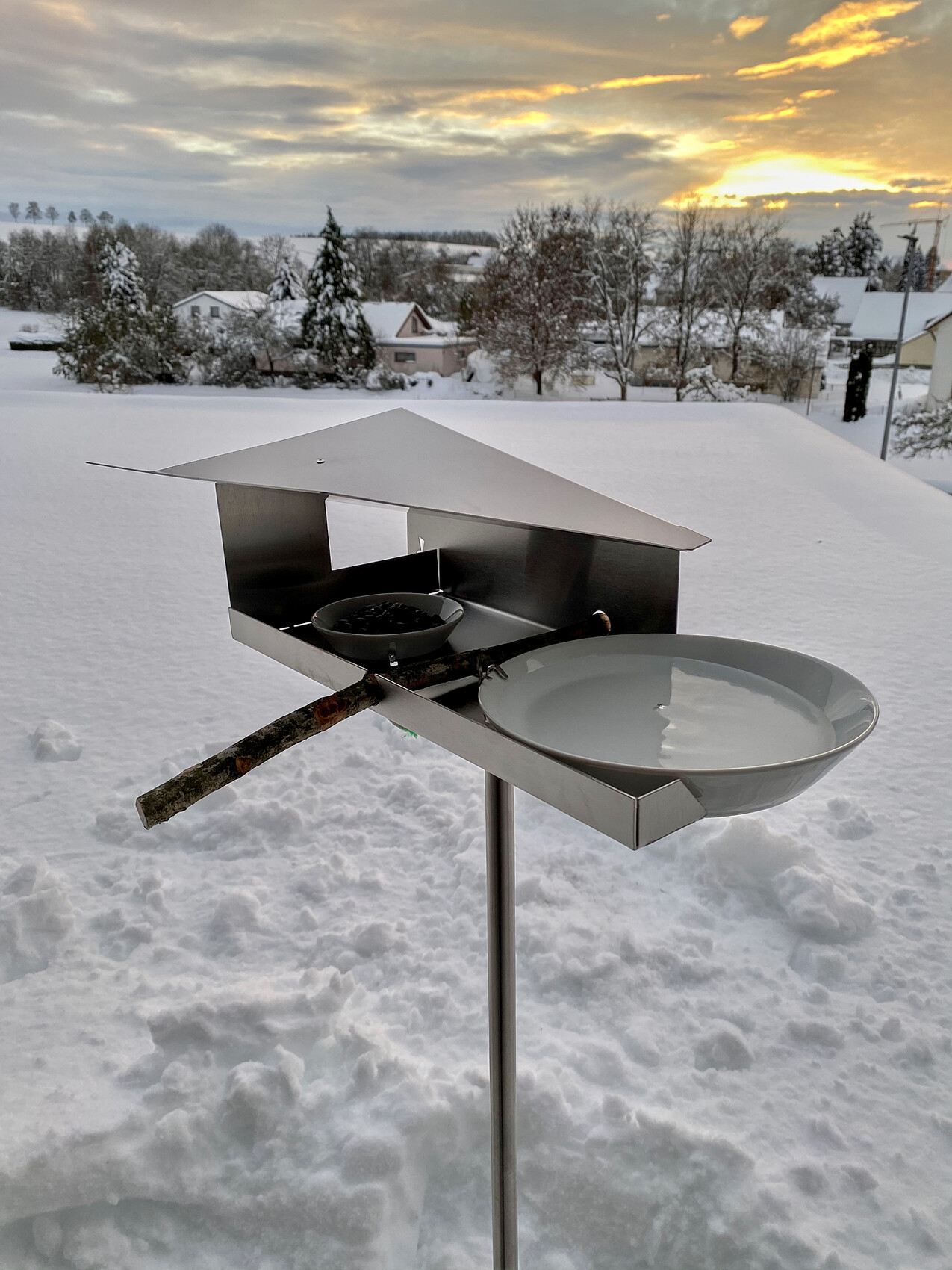Edelstahl-Outdoor-Grill mit Dachhaube, Holzgriff und runder Schale im Schnee, Abendhimmel.